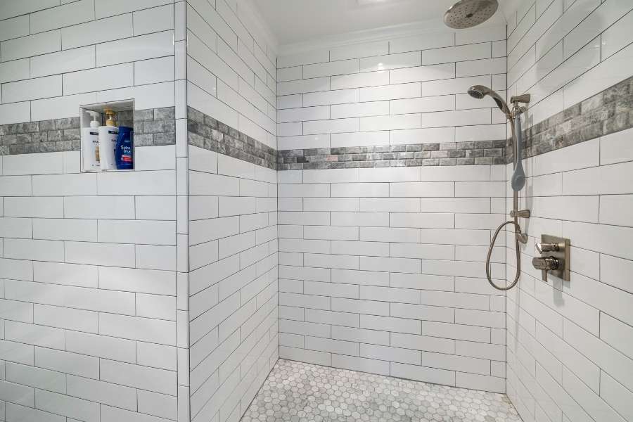 Receveur de douche en mosaïque hexagonale dans une douche carrelée de métro blanc.