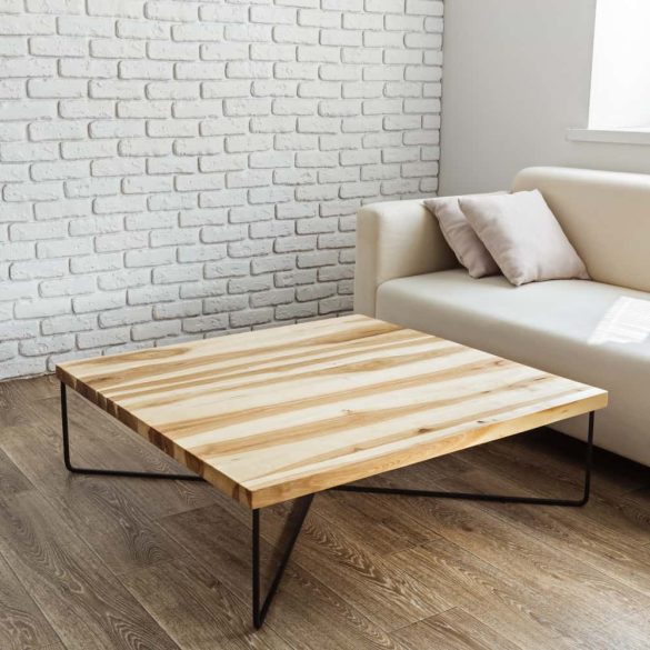 Table basse en bois massif carrée avec pieds en métal noir dans un salon lumineux.
