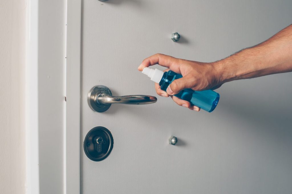 Une personne pulvérise du lubrifiant sur une poignée de porte pour résoudre un problème de serrure bloquee cle ne tourne plus serrurier paris.